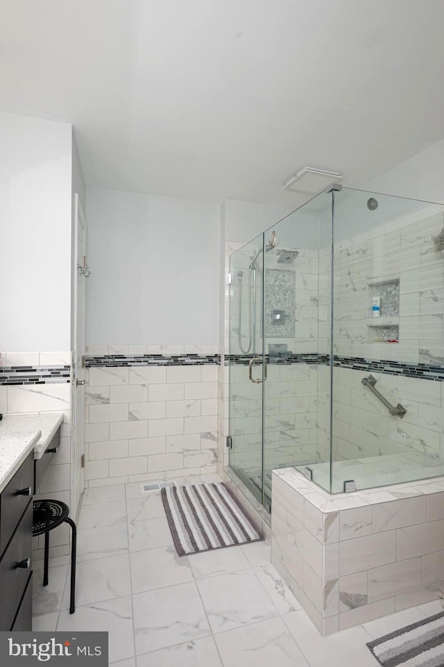 full bath featuring a shower stall, a wainscoted wall, vanity, marble finish floor, and tile walls