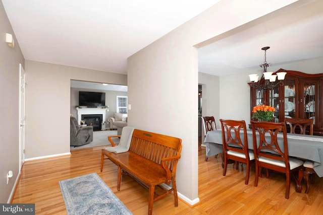 dining space featuring a glass covered fireplace, light wood-type flooring, baseboards, and a chandelier