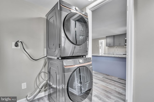 clothes washing area featuring light wood finished floors, a sink, laundry area, and stacked washer and dryer