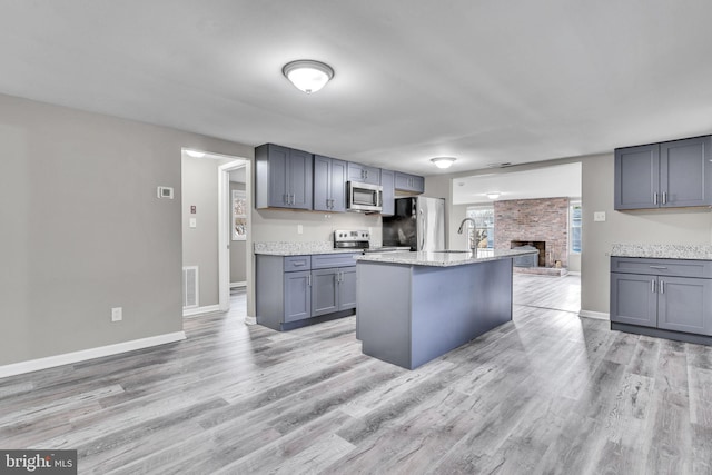 kitchen featuring baseboards, light wood-style flooring, a fireplace, gray cabinets, and stainless steel appliances