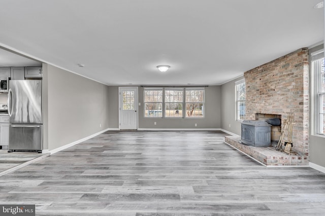 unfurnished living room featuring light wood finished floors, a wood stove, and baseboards