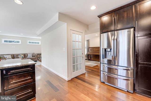 kitchen with dark brown cabinetry, stainless steel fridge, light wood finished floors, and light stone countertops