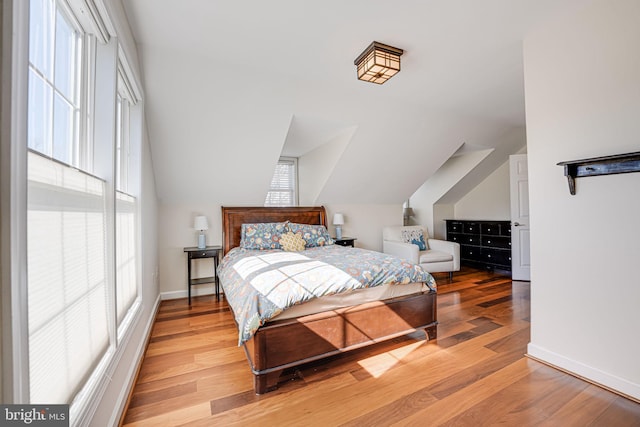 bedroom with light wood-type flooring, baseboards, and vaulted ceiling