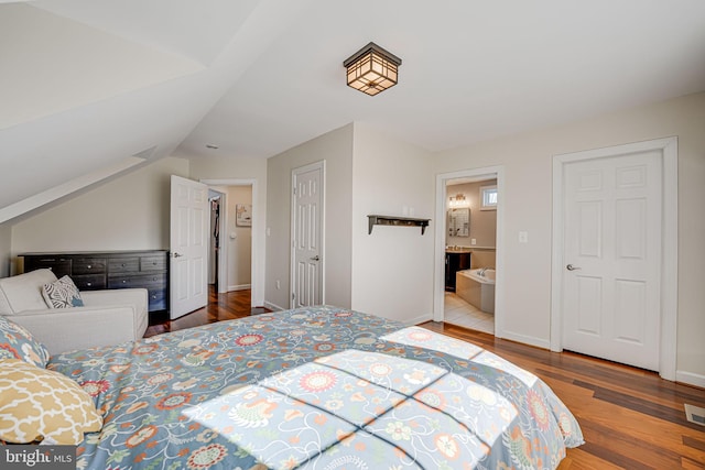 bedroom featuring wood finished floors, visible vents, baseboards, ensuite bath, and lofted ceiling