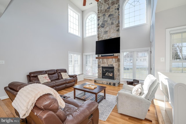 living room featuring light wood-style flooring, a fireplace, a ceiling fan, and a towering ceiling