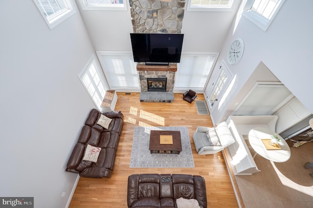 living area with a towering ceiling, a healthy amount of sunlight, wood finished floors, and a fireplace