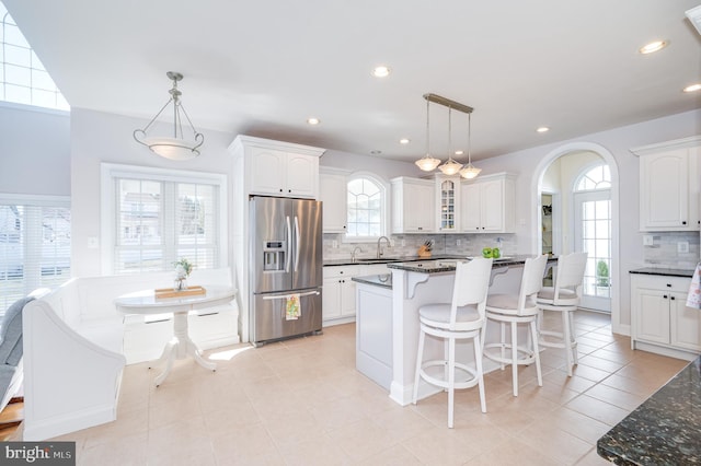 kitchen with stainless steel refrigerator with ice dispenser, a sink, a kitchen breakfast bar, white cabinets, and decorative backsplash