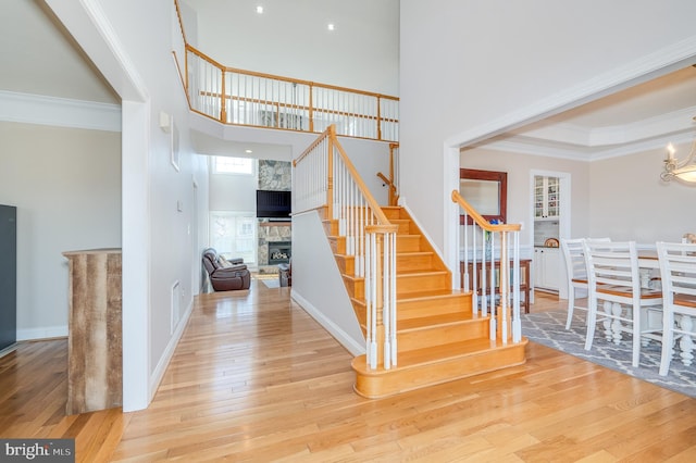 staircase featuring a stone fireplace, ornamental molding, a towering ceiling, and hardwood / wood-style flooring