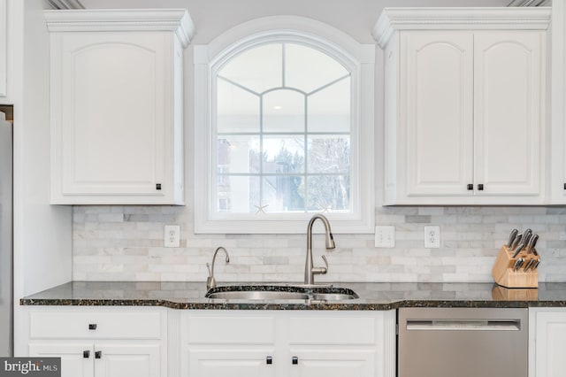 kitchen with stainless steel dishwasher, dark stone countertops, white cabinets, and a sink