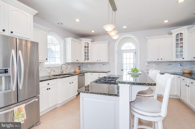 kitchen featuring a center island, glass insert cabinets, dark stone countertops, appliances with stainless steel finishes, and a sink