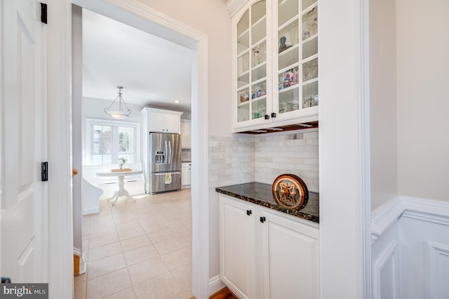 kitchen with glass insert cabinets, stainless steel fridge with ice dispenser, dark stone countertops, light tile patterned flooring, and white cabinets