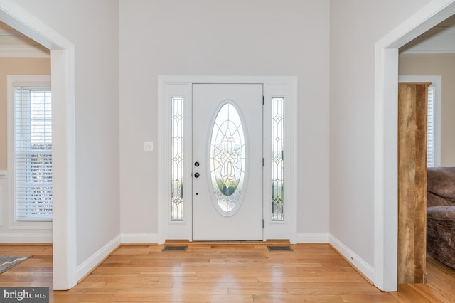 foyer entrance with visible vents, crown molding, light wood-type flooring, and baseboards