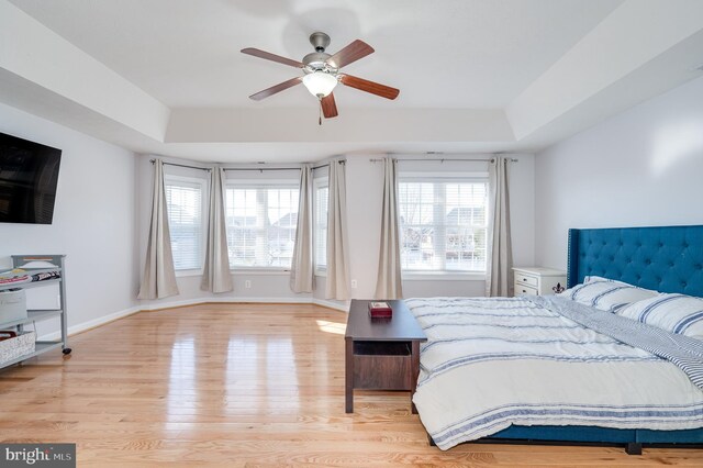 bedroom with a ceiling fan, a raised ceiling, wood finished floors, and baseboards