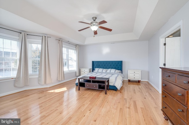 bedroom featuring a tray ceiling, light wood-style flooring, baseboards, and ceiling fan