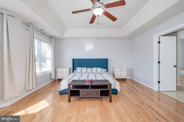 bedroom featuring a ceiling fan, a tray ceiling, baseboards, and light wood-type flooring