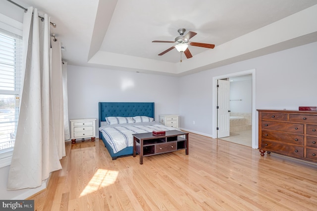 bedroom with baseboards, ensuite bathroom, a tray ceiling, and wood finished floors