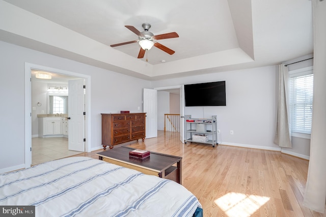 bedroom with a tray ceiling, multiple windows, baseboards, and light wood finished floors