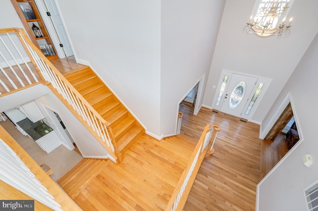 entryway featuring baseboards, wood finished floors, stairs, an inviting chandelier, and a towering ceiling