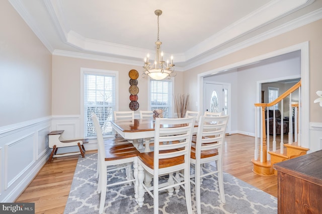 dining area featuring a raised ceiling, light wood-style flooring, a decorative wall, and a chandelier