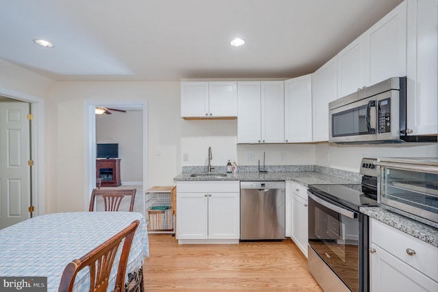 kitchen featuring a ceiling fan, light wood finished floors, a sink, white cabinets, and appliances with stainless steel finishes