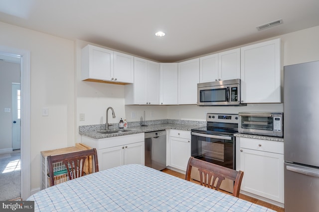 kitchen featuring visible vents, a sink, stainless steel appliances, white cabinets, and a toaster