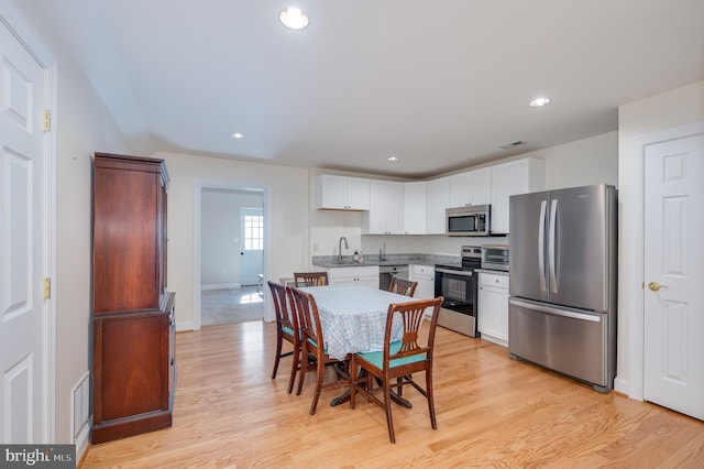 kitchen featuring a sink, white cabinets, light wood-type flooring, and stainless steel appliances