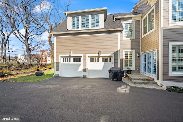 view of side of home with a garage, driveway, and roof with shingles