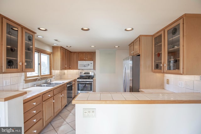 kitchen featuring tile countertops, light tile patterned floors, a peninsula, stainless steel appliances, and a sink