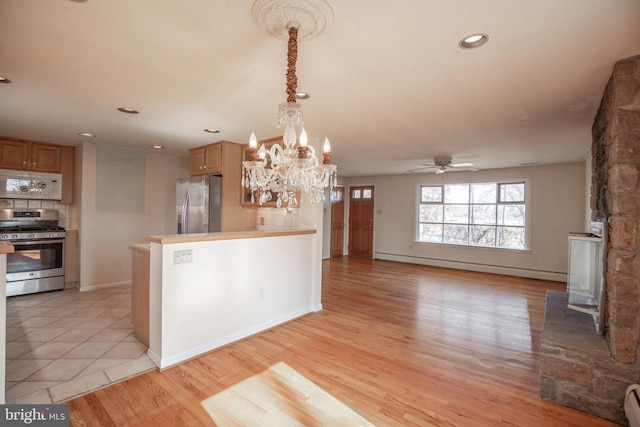 kitchen with light wood finished floors, recessed lighting, appliances with stainless steel finishes, ceiling fan with notable chandelier, and baseboard heating