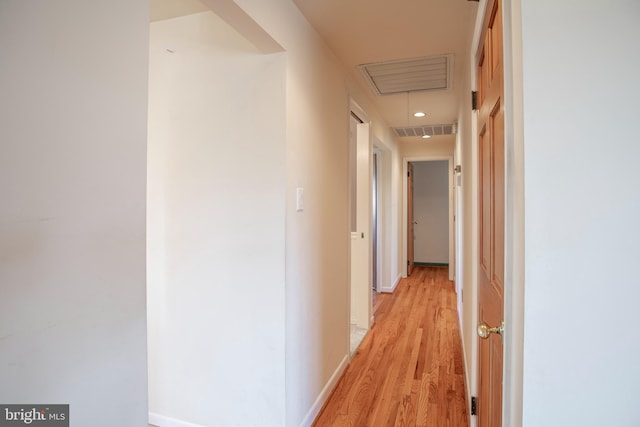 corridor with attic access, baseboards, visible vents, and light wood finished floors