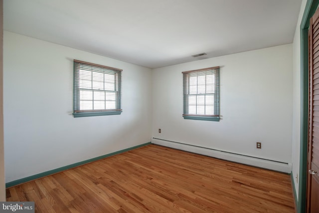 unfurnished room featuring a baseboard heating unit, wood finished floors, visible vents, and baseboards