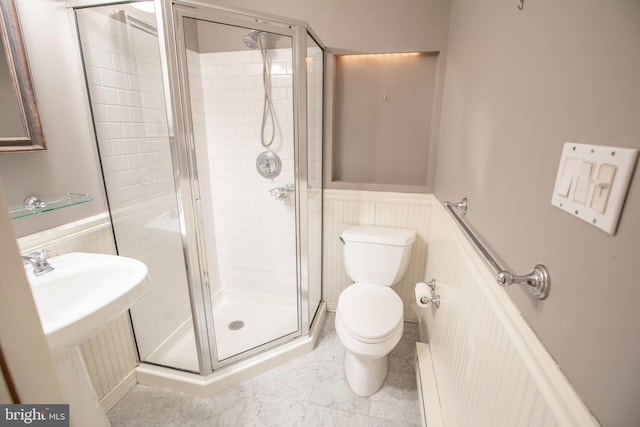 bathroom featuring a wainscoted wall, a shower stall, toilet, and a sink