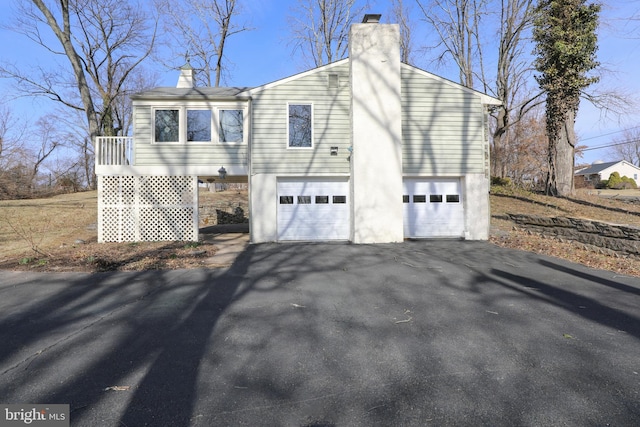 view of home's exterior featuring an attached garage, a chimney, and driveway