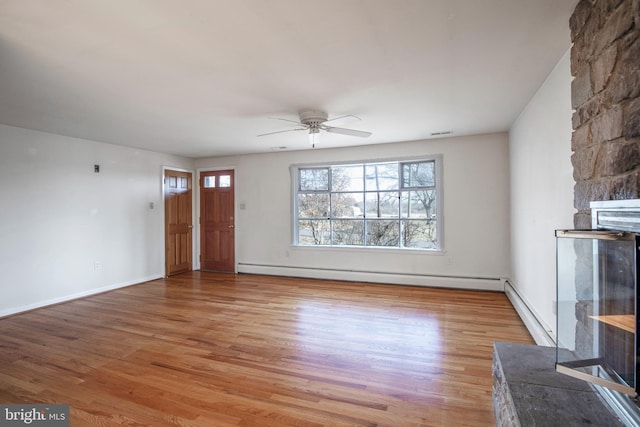 unfurnished living room with a ceiling fan, a stone fireplace, light wood finished floors, a baseboard radiator, and baseboard heating