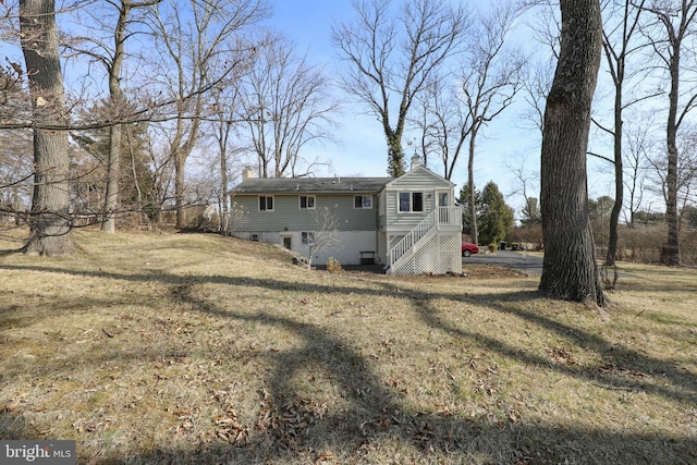 back of property featuring a chimney, stairs, and a yard