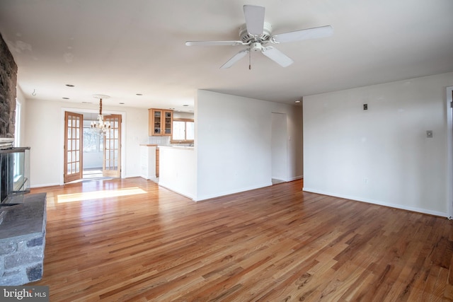 unfurnished living room featuring baseboards, light wood-style floors, and ceiling fan with notable chandelier