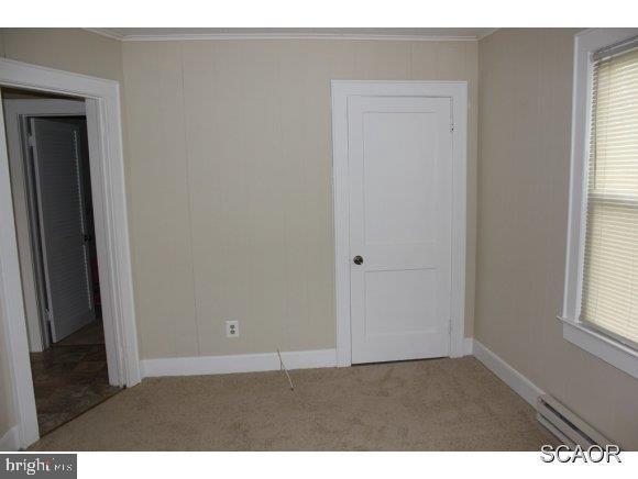 unfurnished bedroom featuring multiple windows, carpet flooring, baseboards, and a baseboard radiator