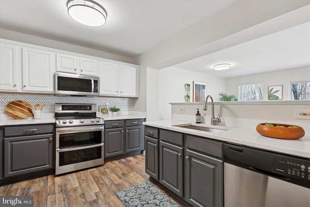 kitchen featuring gray cabinetry, appliances with stainless steel finishes, wood finished floors, white cabinetry, and a sink