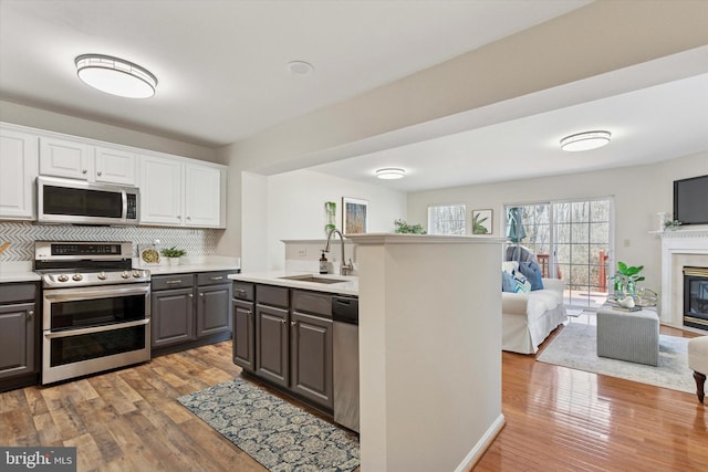 kitchen with gray cabinets, a sink, light countertops, appliances with stainless steel finishes, and open floor plan