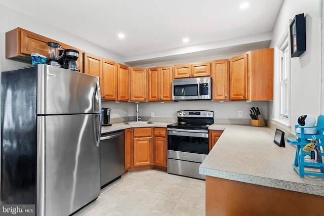 kitchen featuring light countertops, recessed lighting, appliances with stainless steel finishes, brown cabinets, and a sink