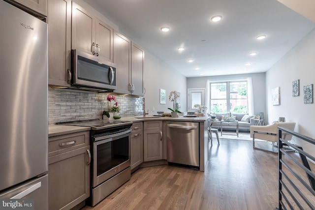 kitchen with light wood finished floors, a peninsula, decorative backsplash, appliances with stainless steel finishes, and open floor plan