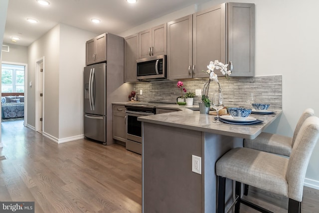 kitchen featuring stainless steel appliances, a peninsula, a breakfast bar, and wood finished floors