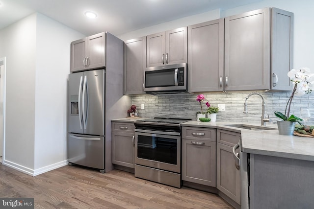 kitchen featuring light wood finished floors, backsplash, gray cabinets, stainless steel appliances, and a sink