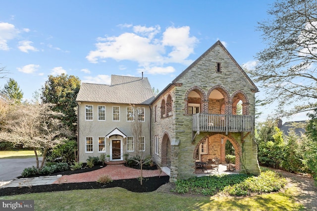 view of front of home featuring brick siding, stone siding, a patio, and a balcony