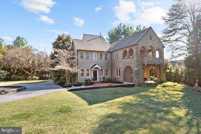 view of front facade featuring brick siding, a front yard, a balcony, stone siding, and driveway