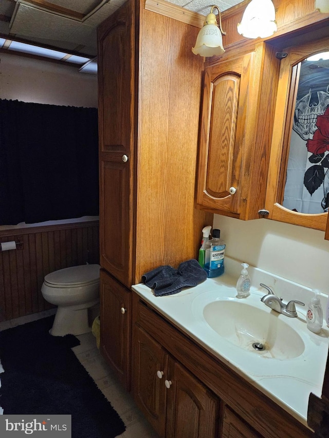 half bath featuring wainscoting, toilet, and vanity