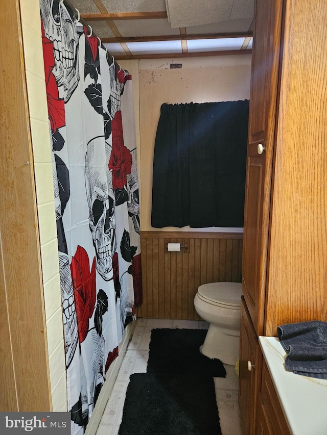 bathroom featuring a shower with shower curtain, wooden walls, and toilet