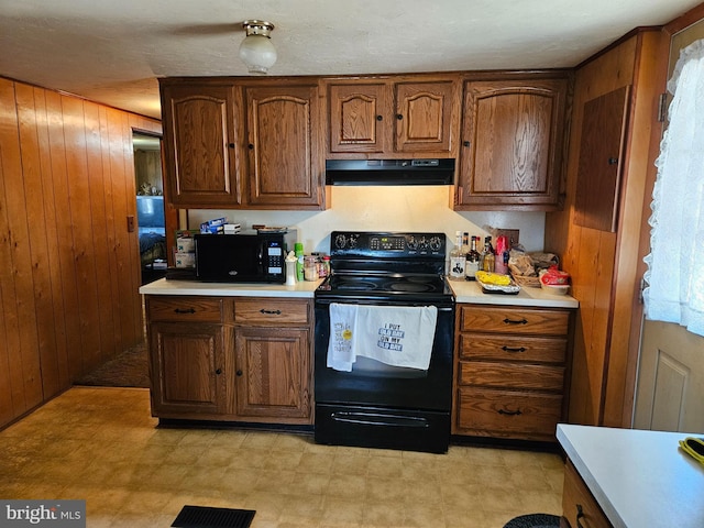 kitchen with wooden walls, visible vents, black appliances, light countertops, and exhaust hood