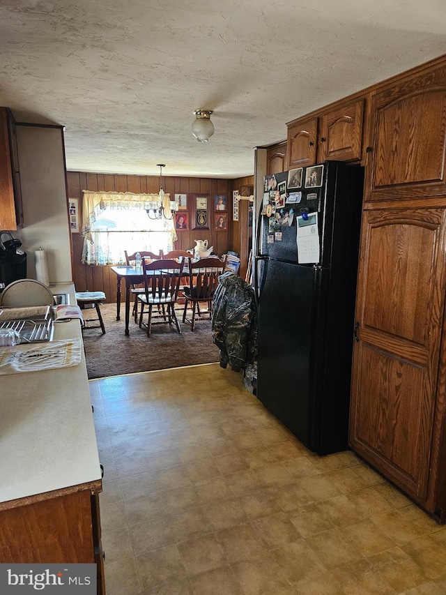 kitchen with decorative light fixtures, wood walls, light floors, brown cabinets, and freestanding refrigerator