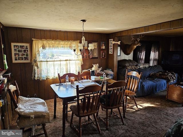 dining room featuring a notable chandelier, carpet, wood walls, and a textured ceiling